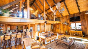 Un chalet spacieux avec de hauts plafonds, des poutres en bois, un grand lustre, une cheminée et un coin salon confortable.