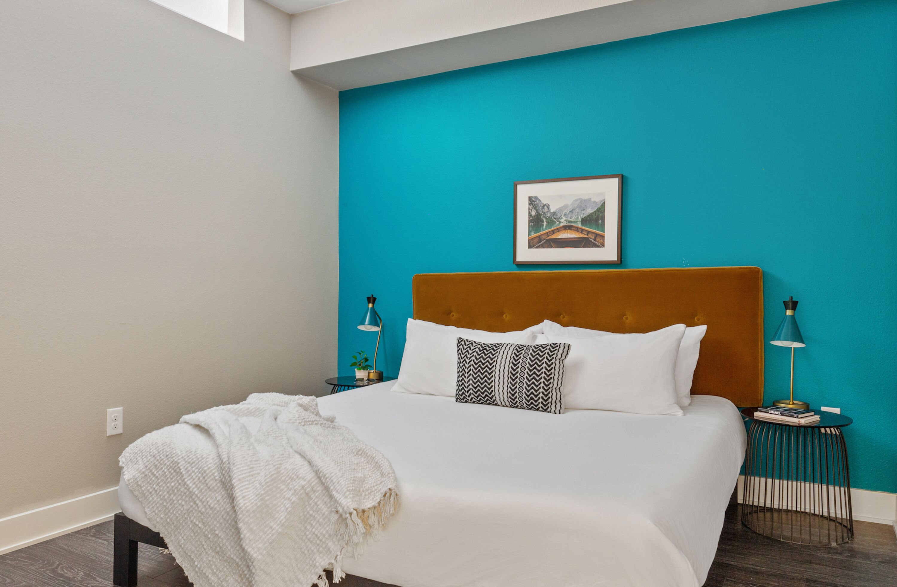 A bedroom with a large bed, a teal accent wall, a framed picture, and bedside lamps.