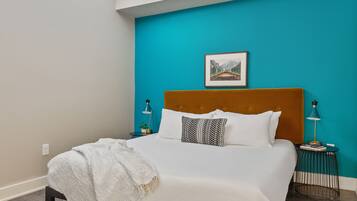 A bedroom with a large bed, a teal accent wall, a framed picture, and bedside lamps.