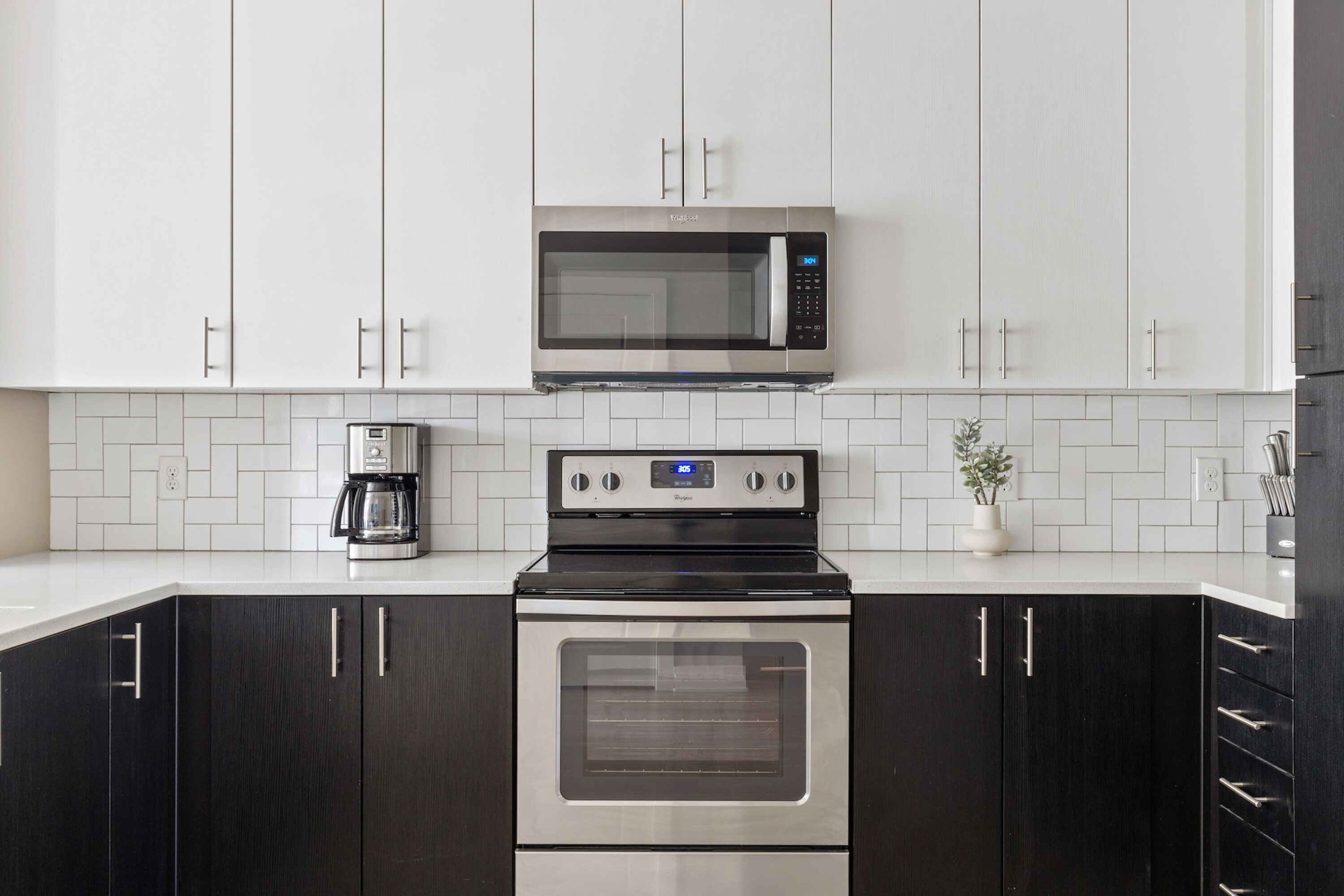 A modern kitchen with white cabinets, a stainless steel microwave, a coffee maker, and a built-in oven.