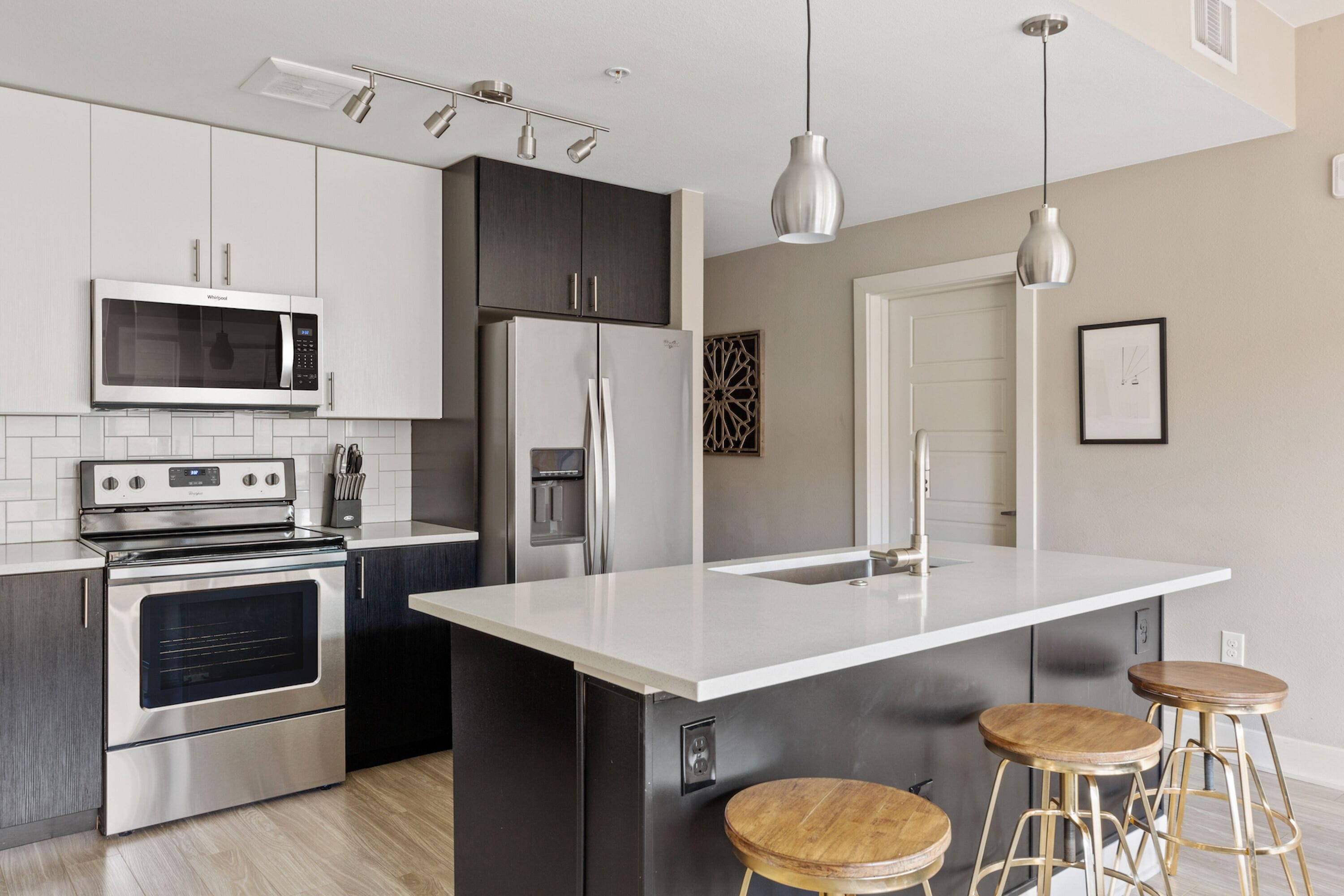 A modern kitchen with stainless steel appliances, a white island with stools, and pendant lighting.