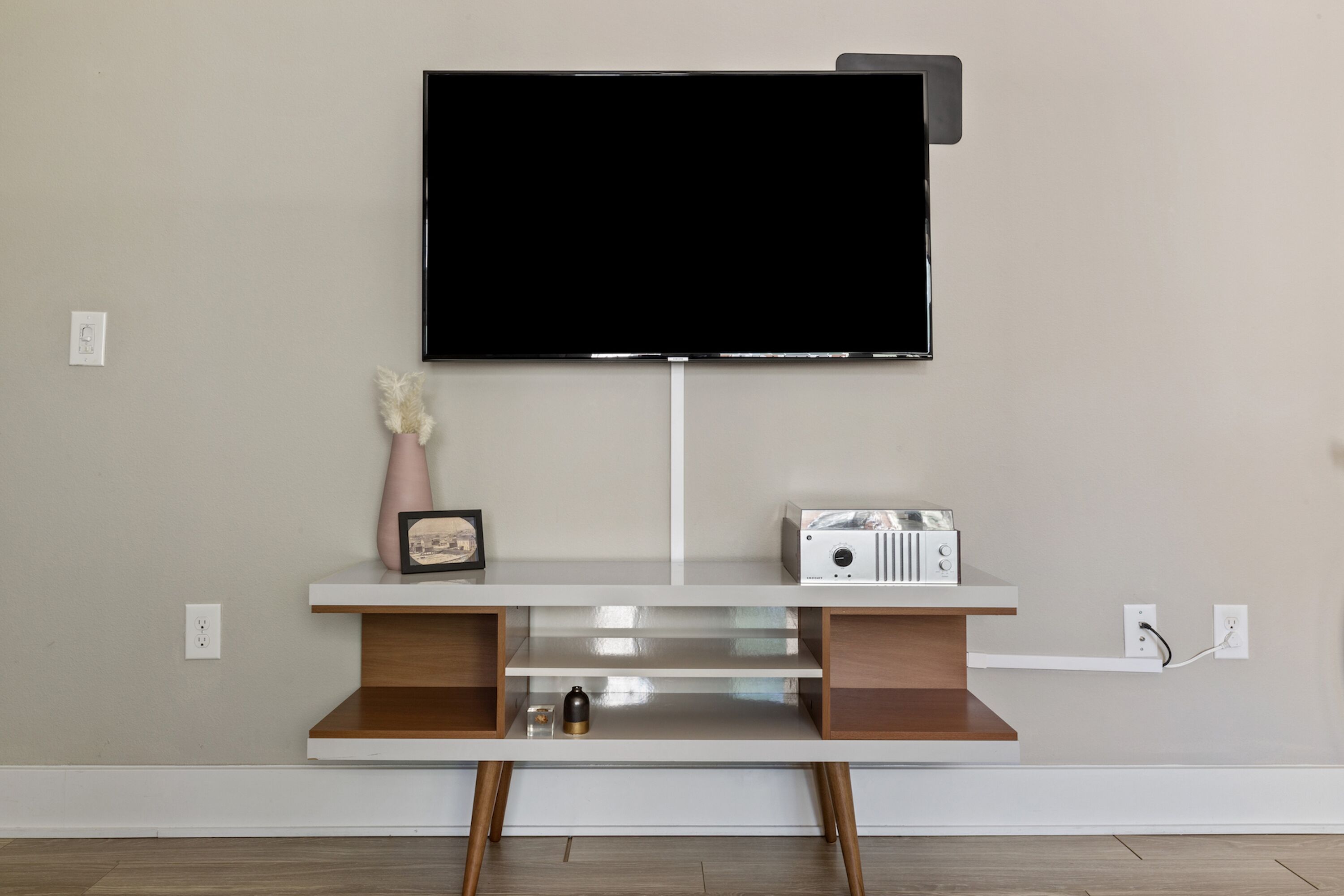 Una sala moderna con un televisor de pared, un mueble blanco para equipo audiovisual y una radio pequeña.