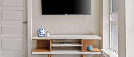 A modern living room with a flat-screen TV mounted on the wall, a white console table with shelves, and a window with a view.