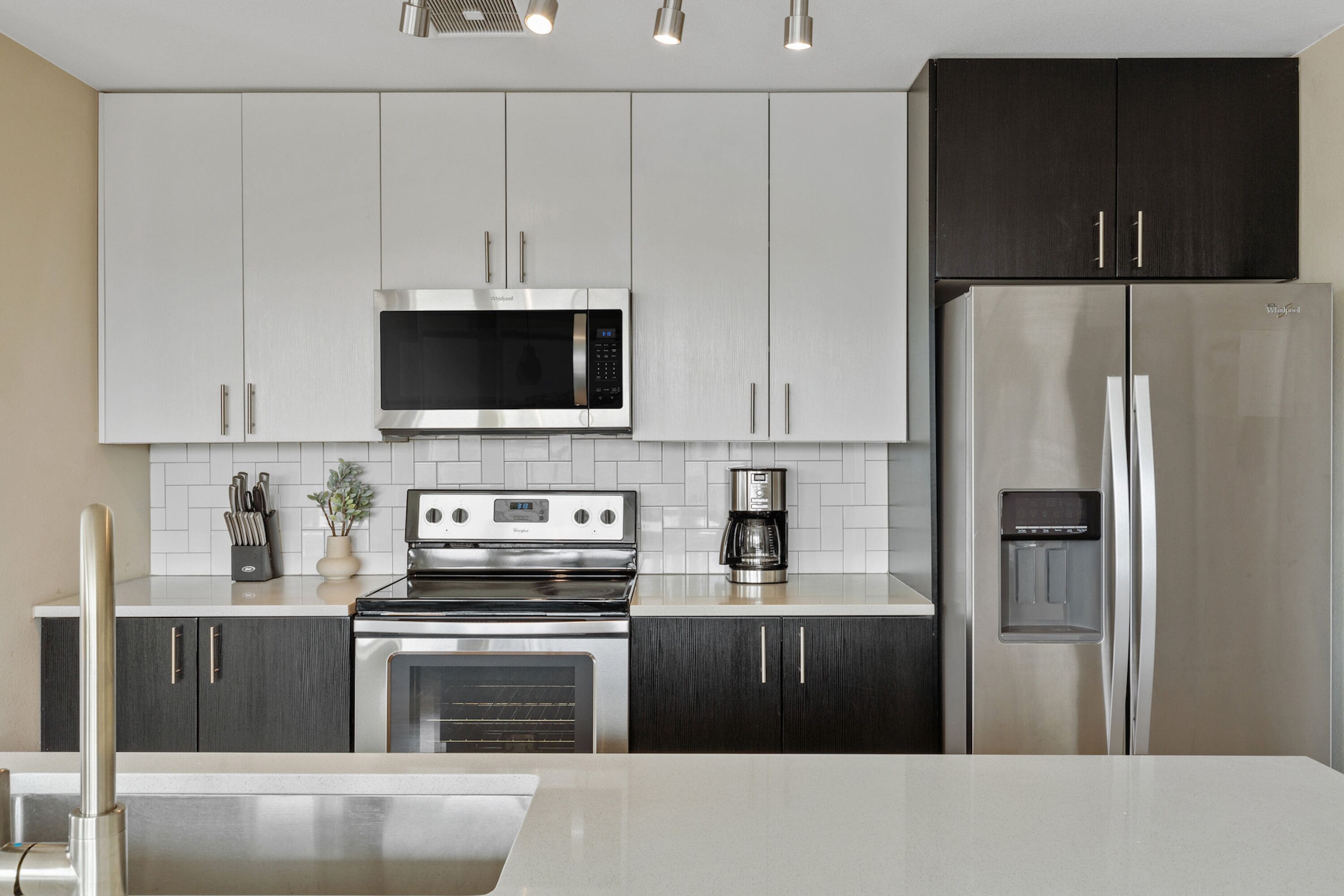 A modern kitchen with stainless steel appliances, white and dark wood cabinets, and a white countertop.