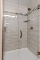 Ducha con paredes de azulejos blancos, cabezal de ducha de mano y grifo empotrado.