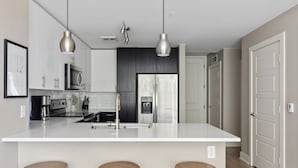 A modern kitchen with white countertops, stainless steel appliances, and wooden stools. - Kasa Union Station Denver (Denver)