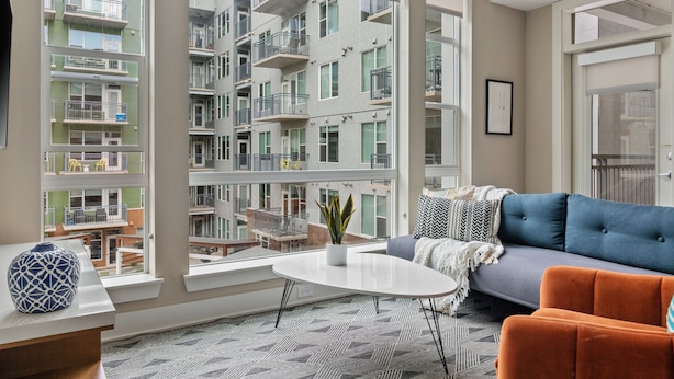A modern apartment with large windows, a sofa, a coffee table, and a view of neighboring buildings. - Kasa Union Station Denver (Denver)