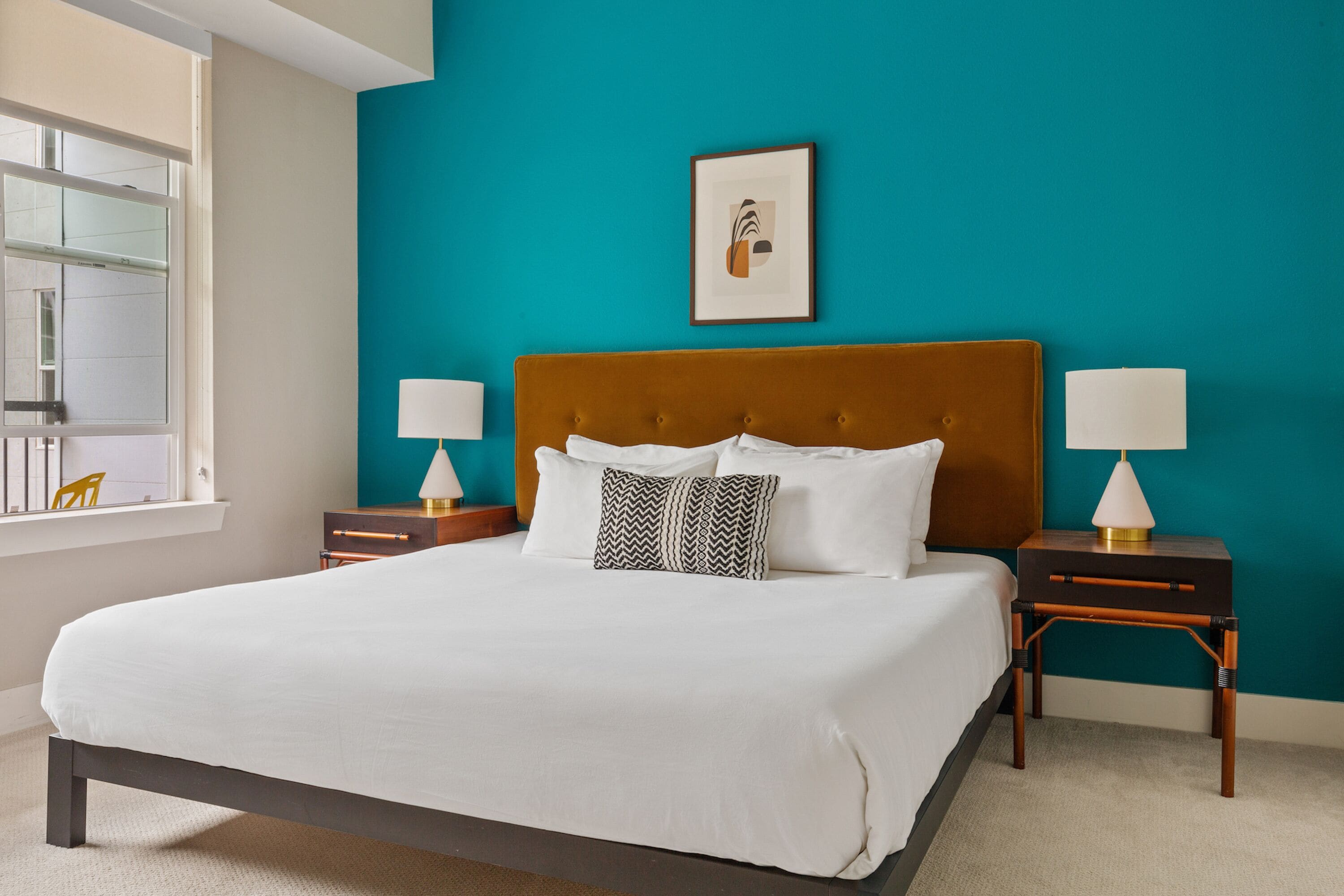 A bedroom with a large bed, two bedside tables, a window, and a teal-colored wall.