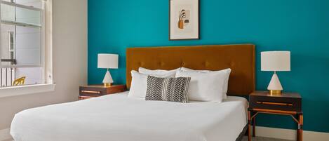 A bedroom with a large bed, two bedside tables, a window, and a teal-colored wall.