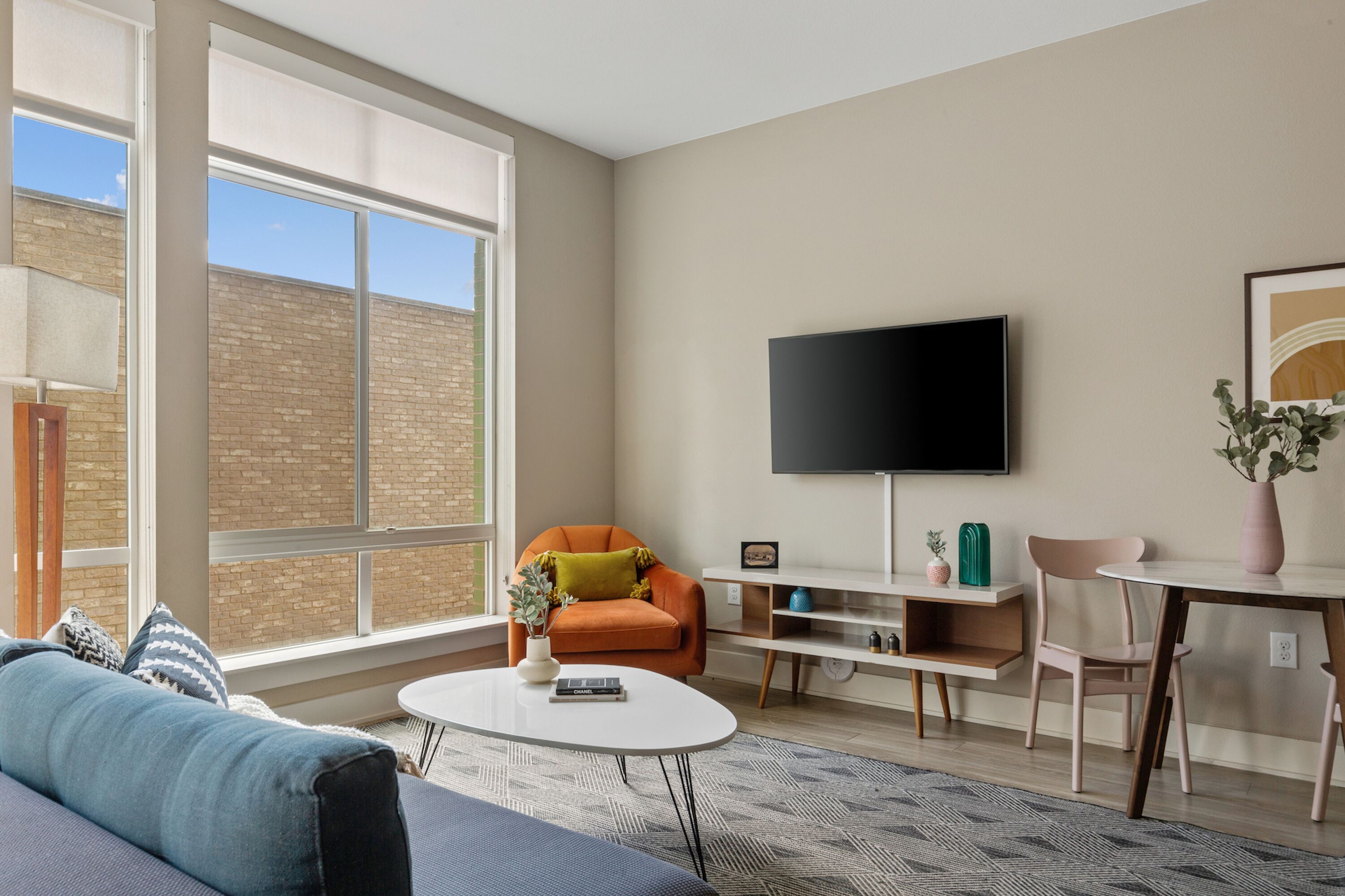 Uma sala de estar moderna com uma janela ampla, uma TV de tela plana, um sofá, uma mesa de centro e um espaço para refeições.