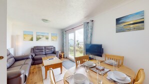 Un salon avec un canapé, une table à manger dressée pour deux personnes, un téléviseur et un tableau accroché au mur.