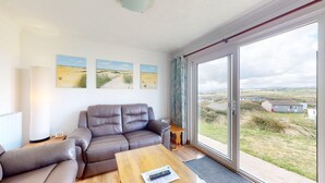 Un salon moderne avec un canapé en cuir, une table basse en bois et une grande porte-fenêtre coulissante donnant sur un paysage extérieur magnifique.