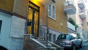 Un edificio de dos pisos con fachada amarilla, una reja negra y una escalera que conduce a la entrada.