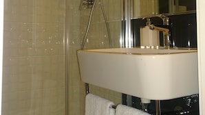 Un baño moderno con cabina de ducha de vidrio, lavabo blanco y un espejo grande.
