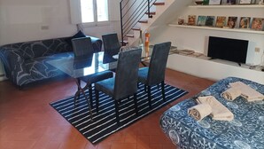 A modern living room with a glass dining table, dark patterned sofa, and a staircase with wooden steps.