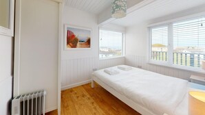 Un dormitorio con una cama individual, paredes blancas, suelo de madera, un radiador y una ventana con persianas.