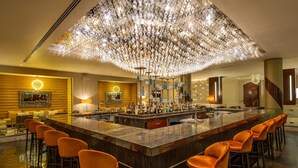 A bar area with a large, ornate chandelier, multiple bar stools, and a variety of bottles on the counter.