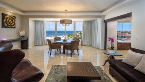 A modern hotel room with a dining area, a sofa, a coffee table, and a view of the ocean.