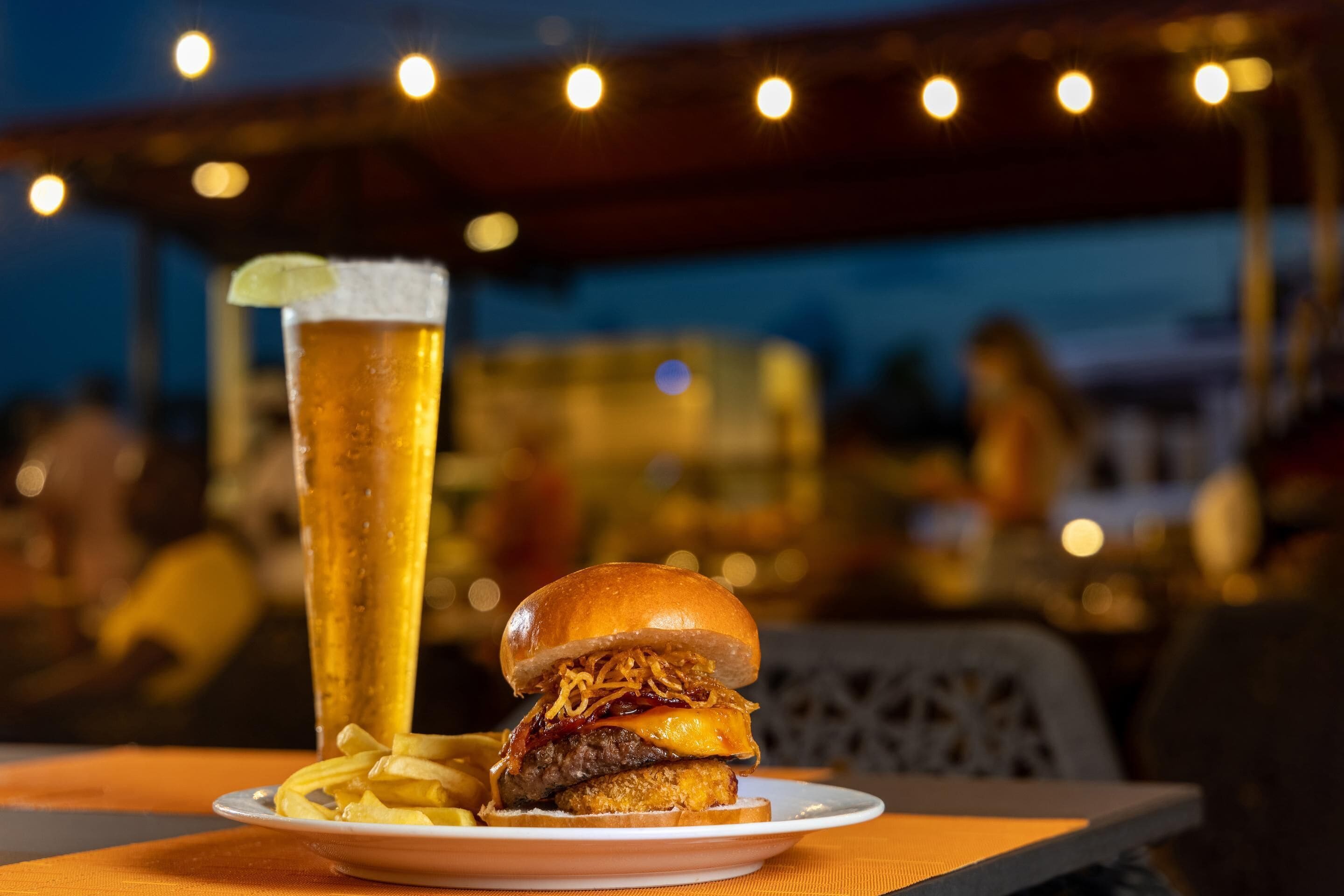 Et måltid med en burger og pommes frites på en tallerken, et højt fadølglas og et bord med en stol.