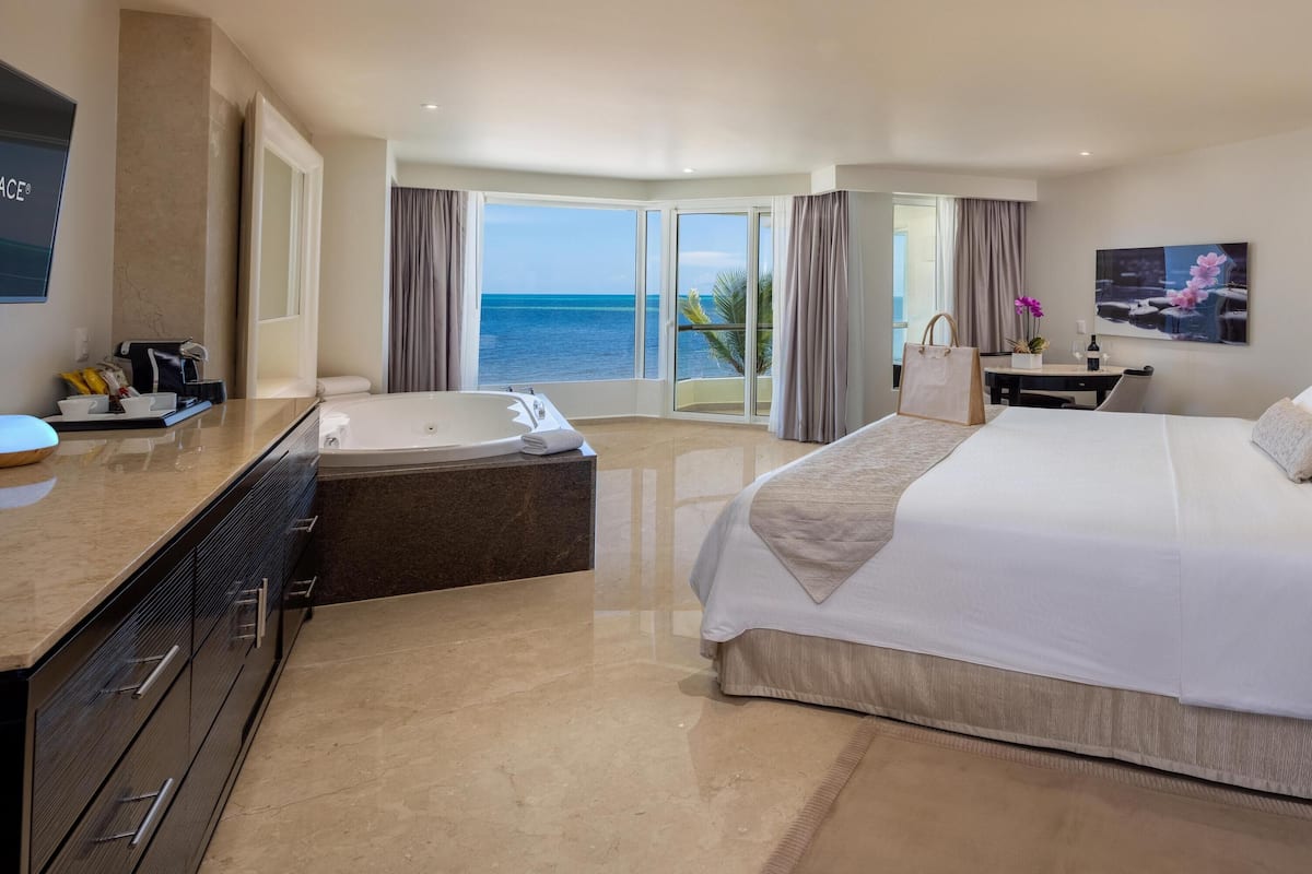 Habitación de hotel con una cama grande, un escritorio, una bañera y vista al océano.