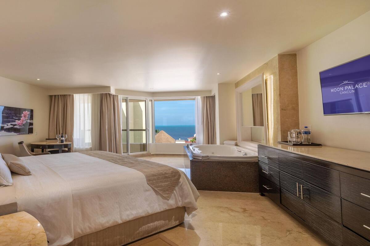 Una habitación de hotel moderna con una cama grande, una zona de estar, una bañera y vistas al océano.