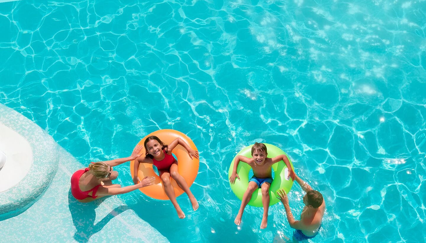 A swimming pool with clear blue water and three people on inflatable rings.