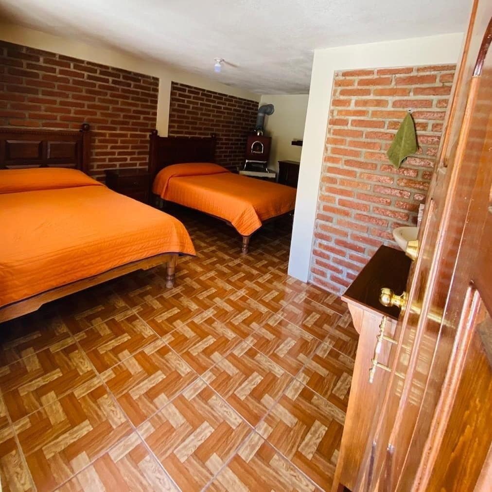 Una habitación con dos camas, piso de madera, pared de ladrillo y un pequeño armario de madera.
