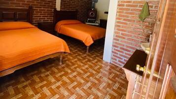 Una habitación con dos camas, piso de madera, pared de ladrillo y un pequeño armario de madera.