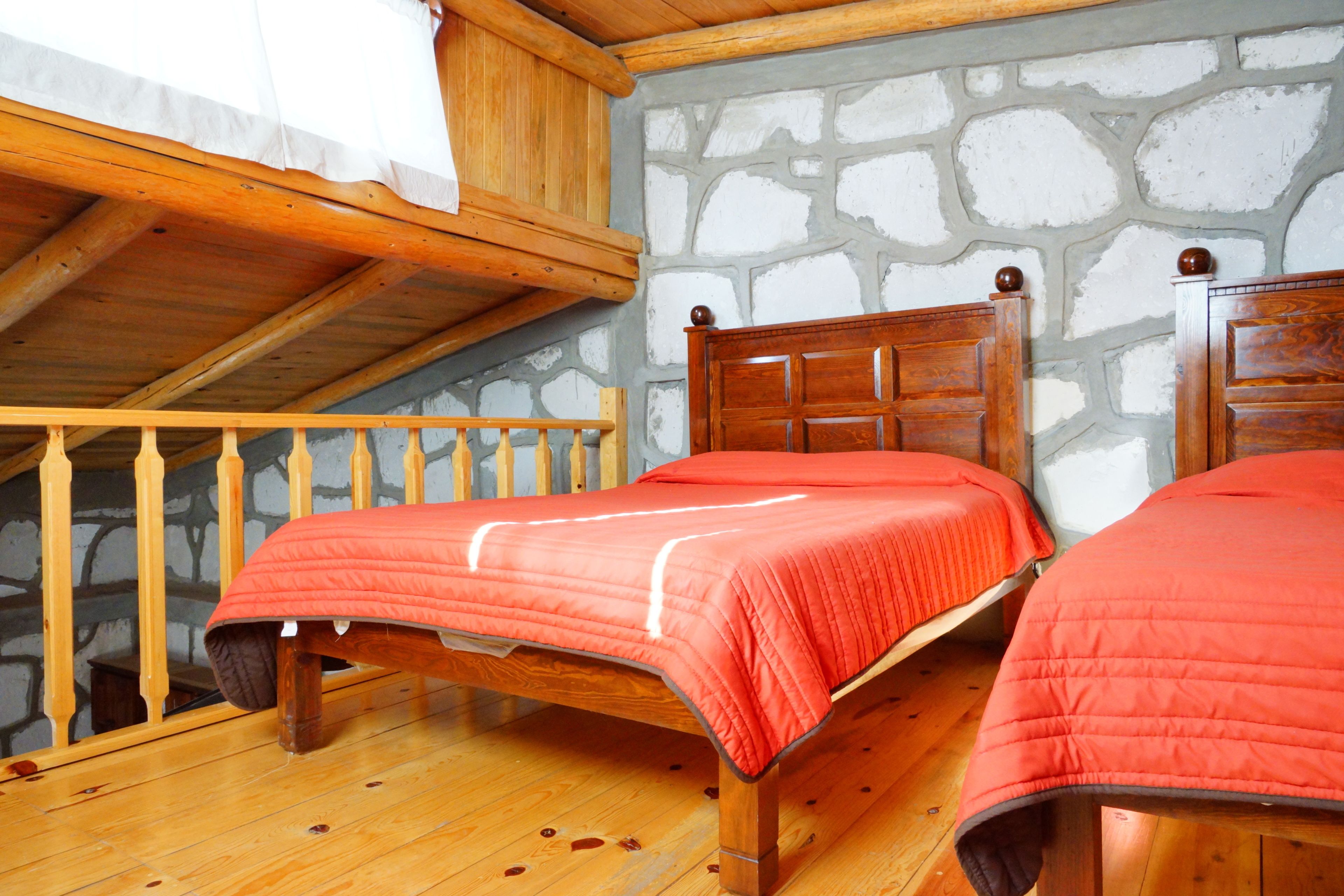 A wooden bed with a red bedspread in a room with stone walls and a wooden ceiling.