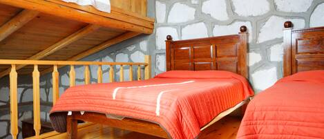 A wooden bed with a red bedspread in a room with stone walls and a wooden ceiling.
