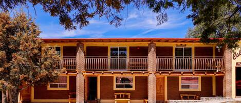 A two-story building with a balcony, wooden benches, and a brick facade.