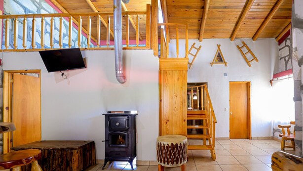 A rustic wooden interior with a wooden staircase, a fireplace, a television, and a wooden bench. - Cabañas Las Gemelas Barrancas del Cobre (Urique)