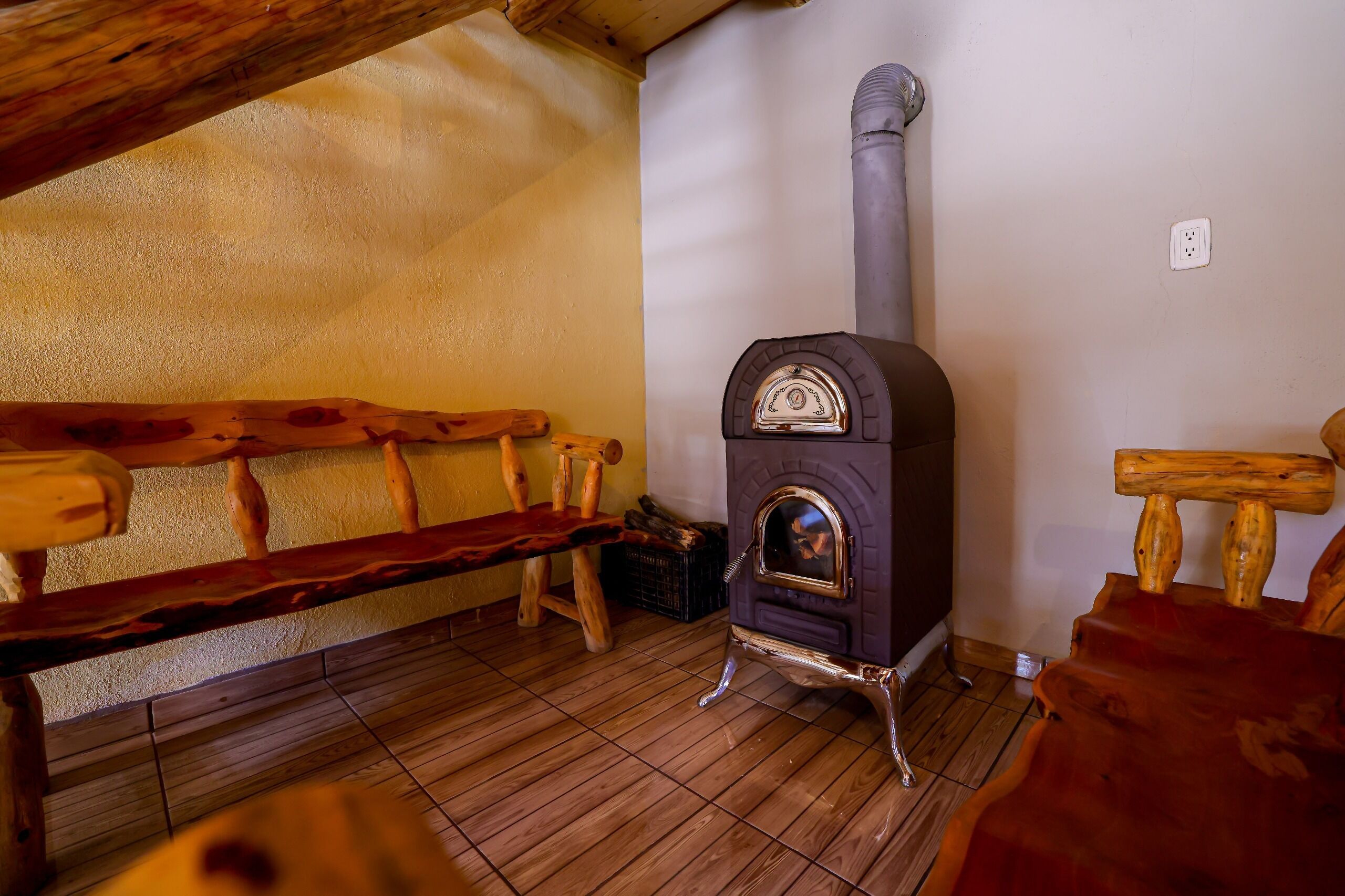 A wooden bench, a wood-burning stove, and a wooden chair in a room with a tiled floor.