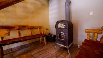 A wooden bench, a wood-burning stove, and a wooden chair in a room with a tiled floor.