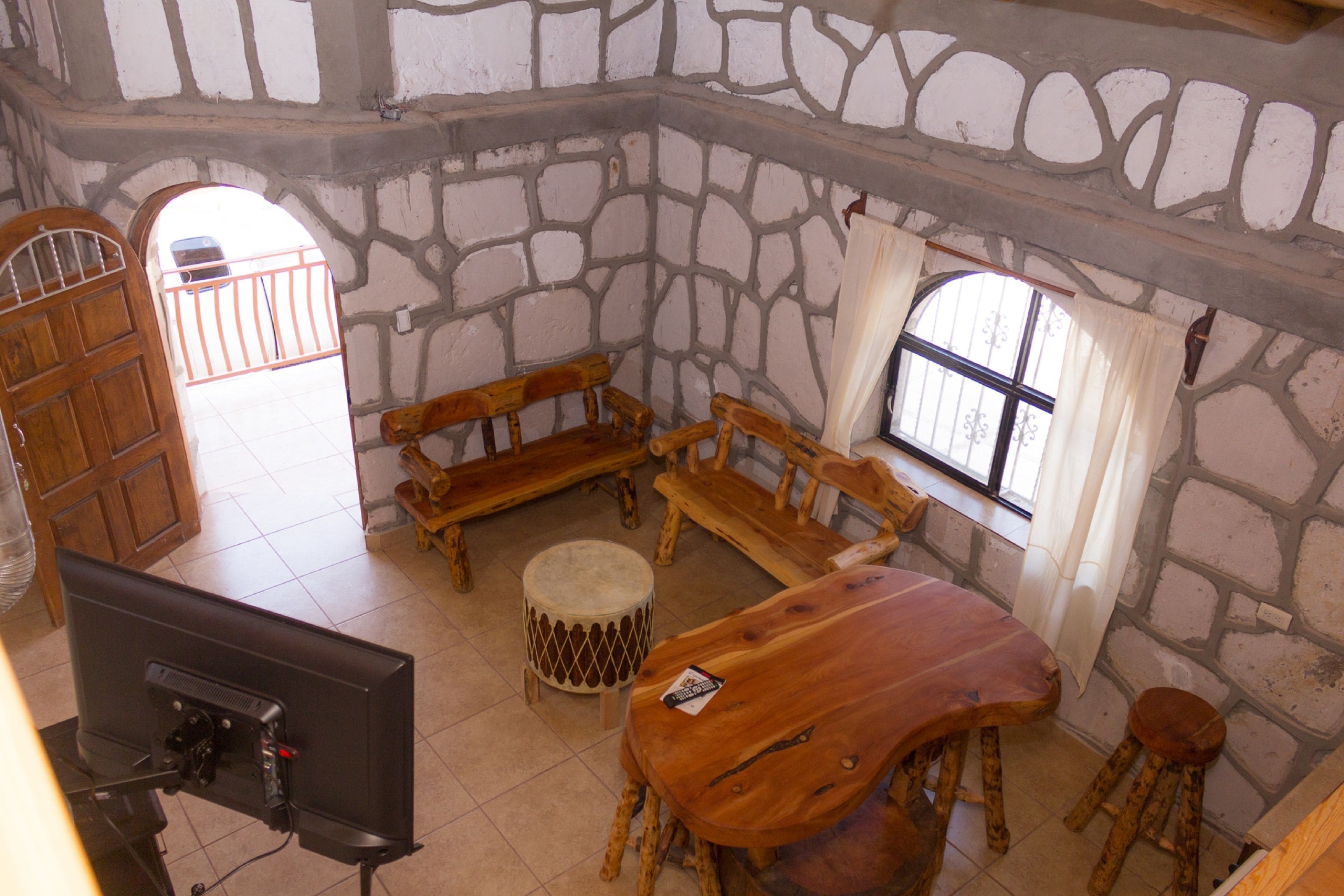 A stone-walled room with a wooden table, benches, and a television.