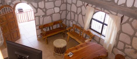 A stone-walled room with a wooden table, benches, and a television.