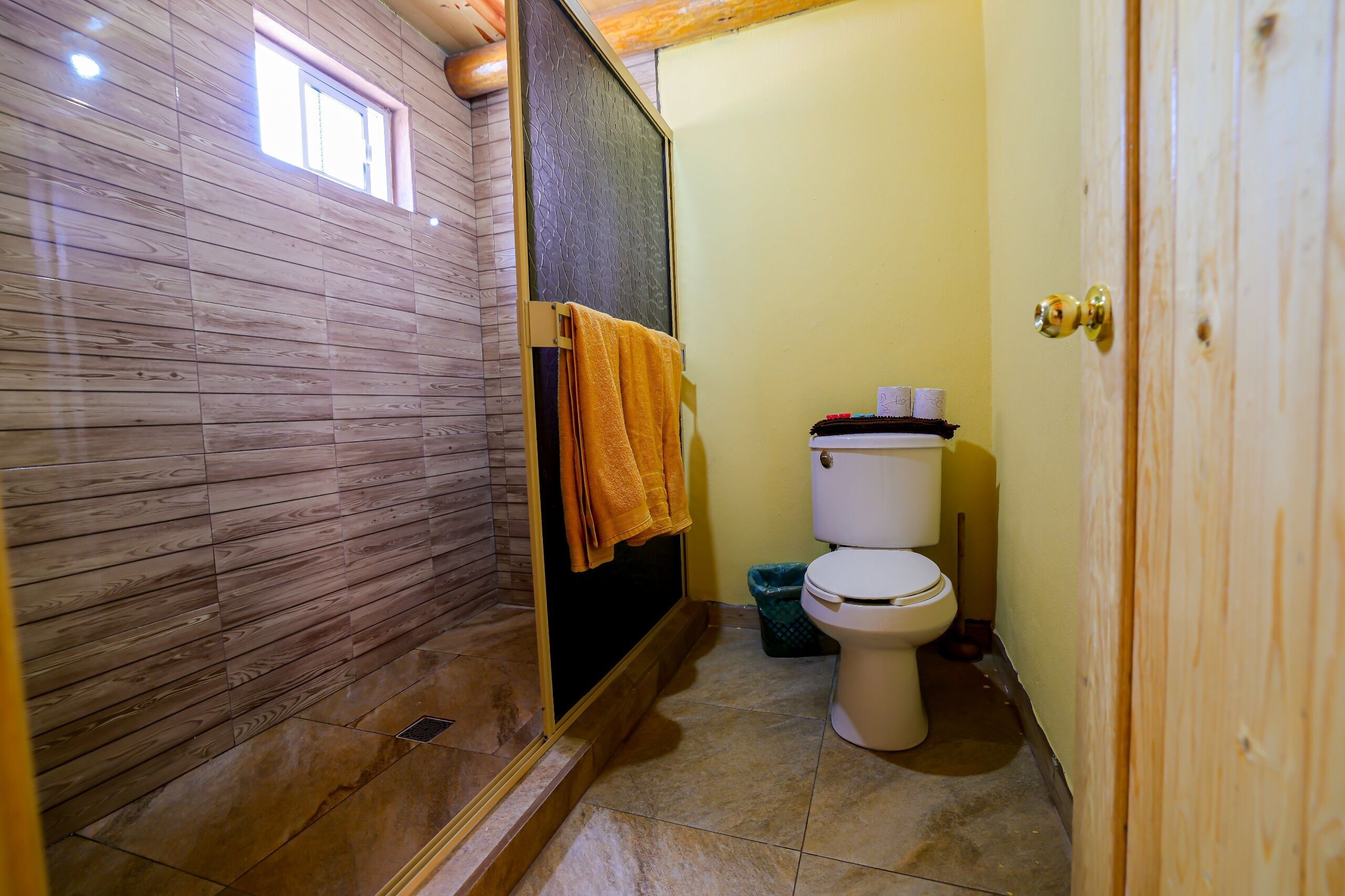A bathroom with a wooden wall, a shower, a toilet, and a towel rack.