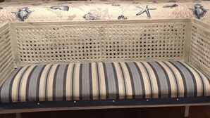 A bed with a floral and starfish patterned bedspread, a striped bench, and a wooden floor.