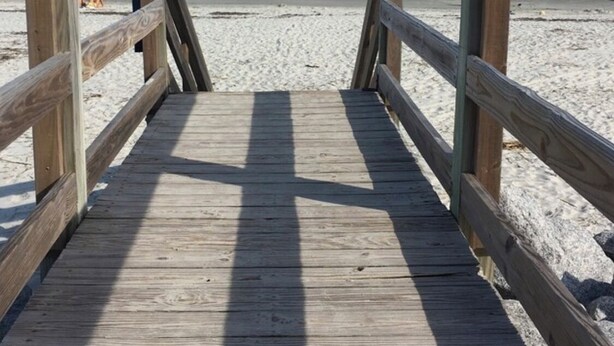 A wooden boardwalk leading to a sandy beach with the ocean in the background.