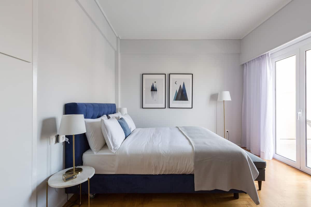 A bedroom with a bed, bedside lamps, a small table, and two framed pictures on the wall.