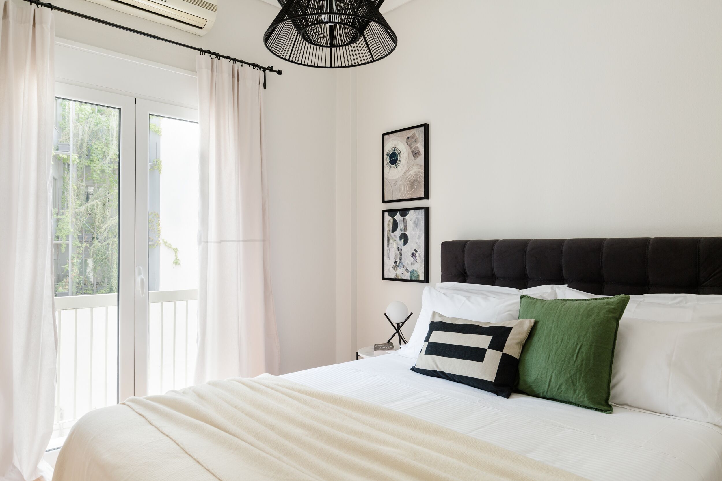 A bedroom with a large bed, a window with curtains, a ceiling fan, and two framed pictures on the wall.