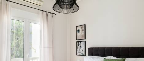 Une chambre à coucher avec un grand lit, une fenêtre avec des rideaux, un ventilateur de plafond et deux tableaux encadrés accrochés au mur.