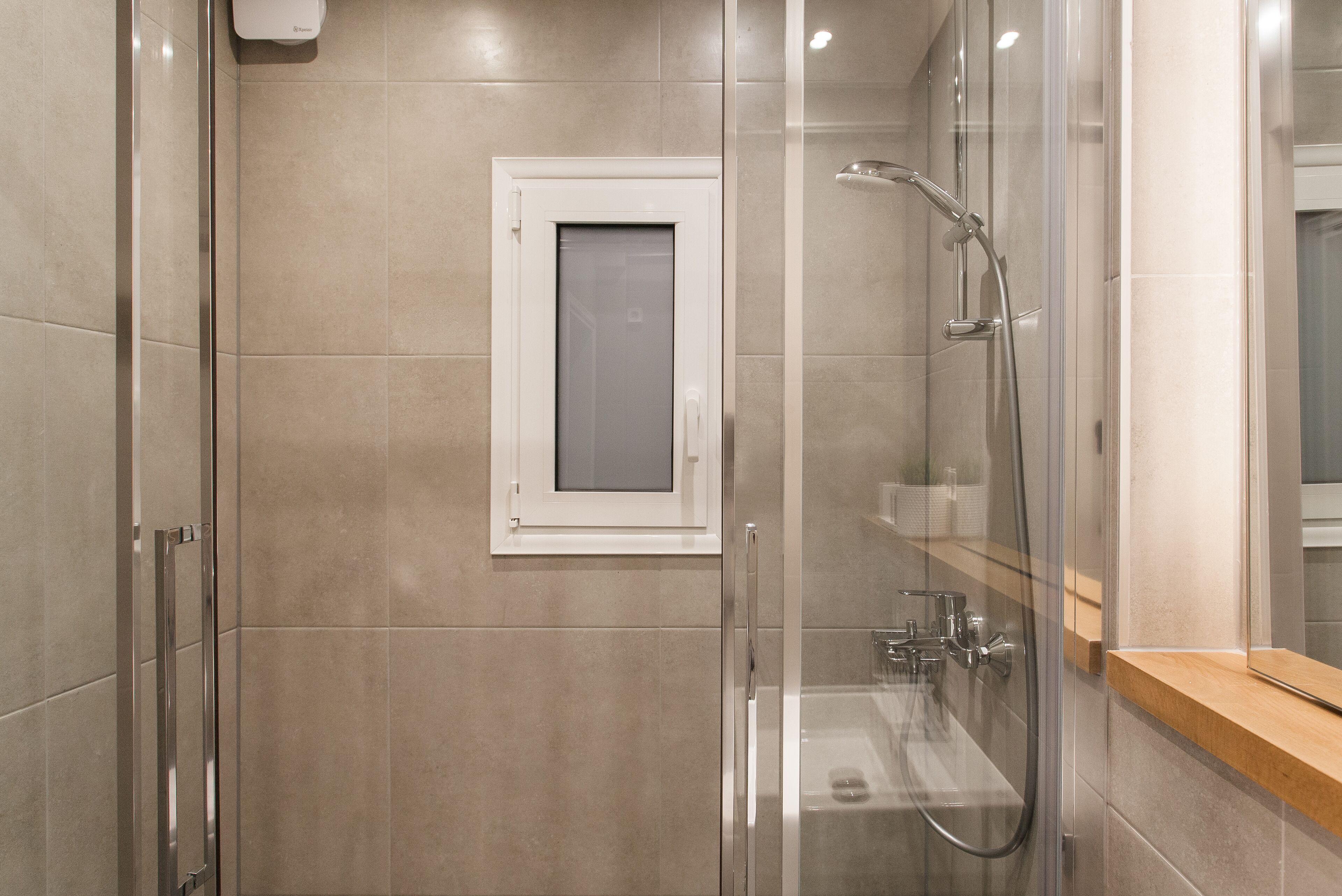 Een moderne badkamer met een douchecabine van glas, een klein raam en een houten aanrecht.