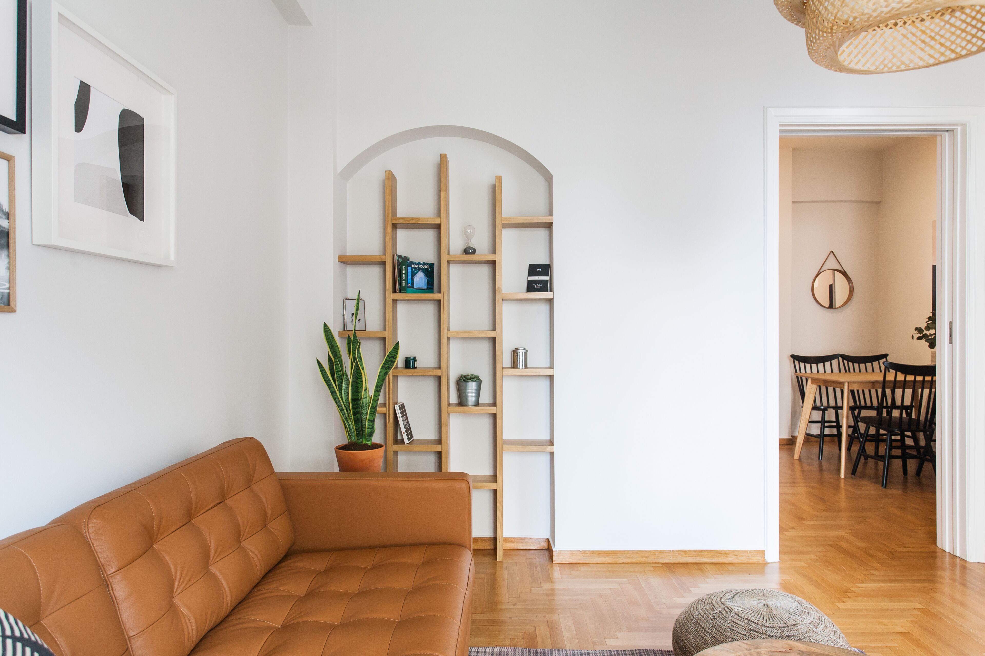 A modern living room with a brown leather sofa, a wooden bookshelf, and a dining area with a wooden table and chairs.