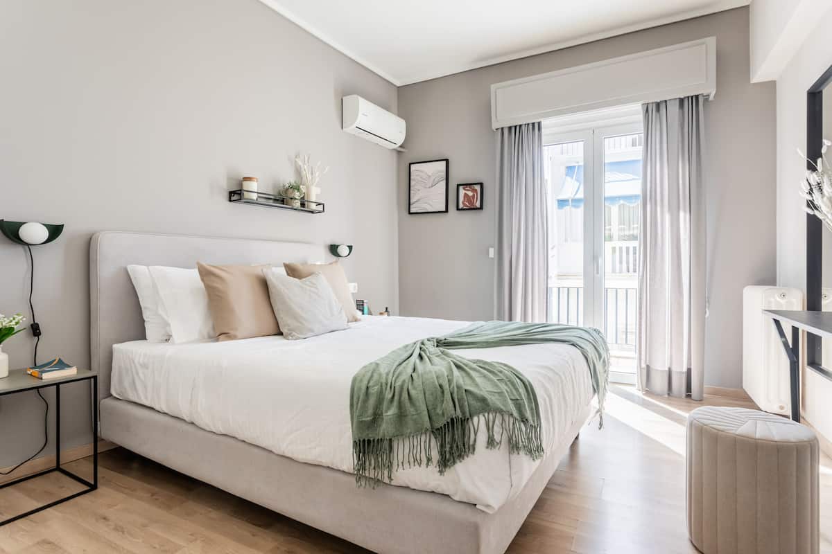 A modern bedroom with a large bed, bedside tables, a nightstand, a window with curtains, and a view of the outside.