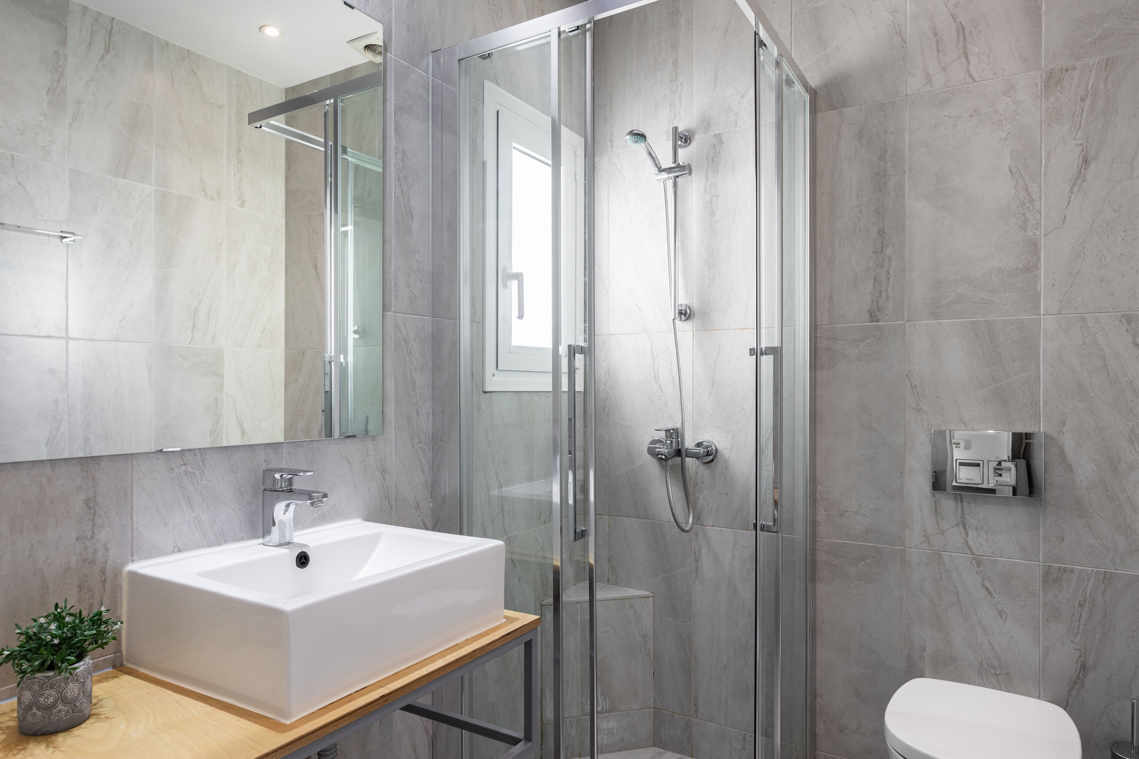 A modern bathroom with a white sink, a glass shower enclosure, and a toilet.