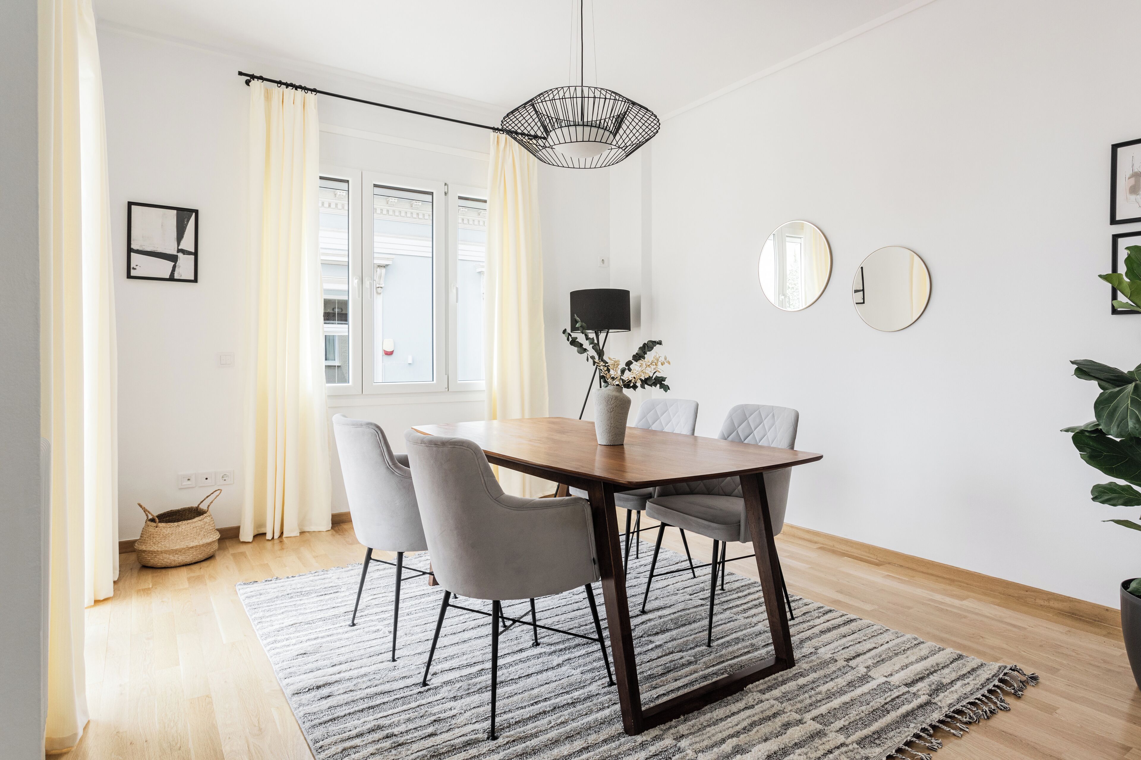 Un comedor con una mesa de madera, sillas grises, una lámpara colgante negra y una alfombra.