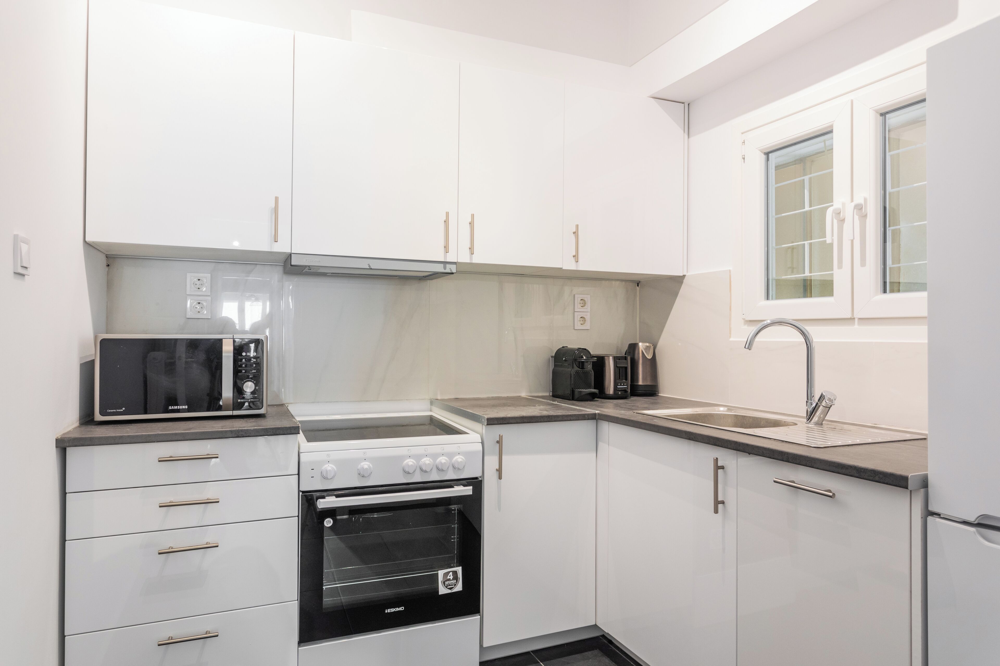 A modern kitchen with white cabinets, a built-in oven, a microwave, and a sink.