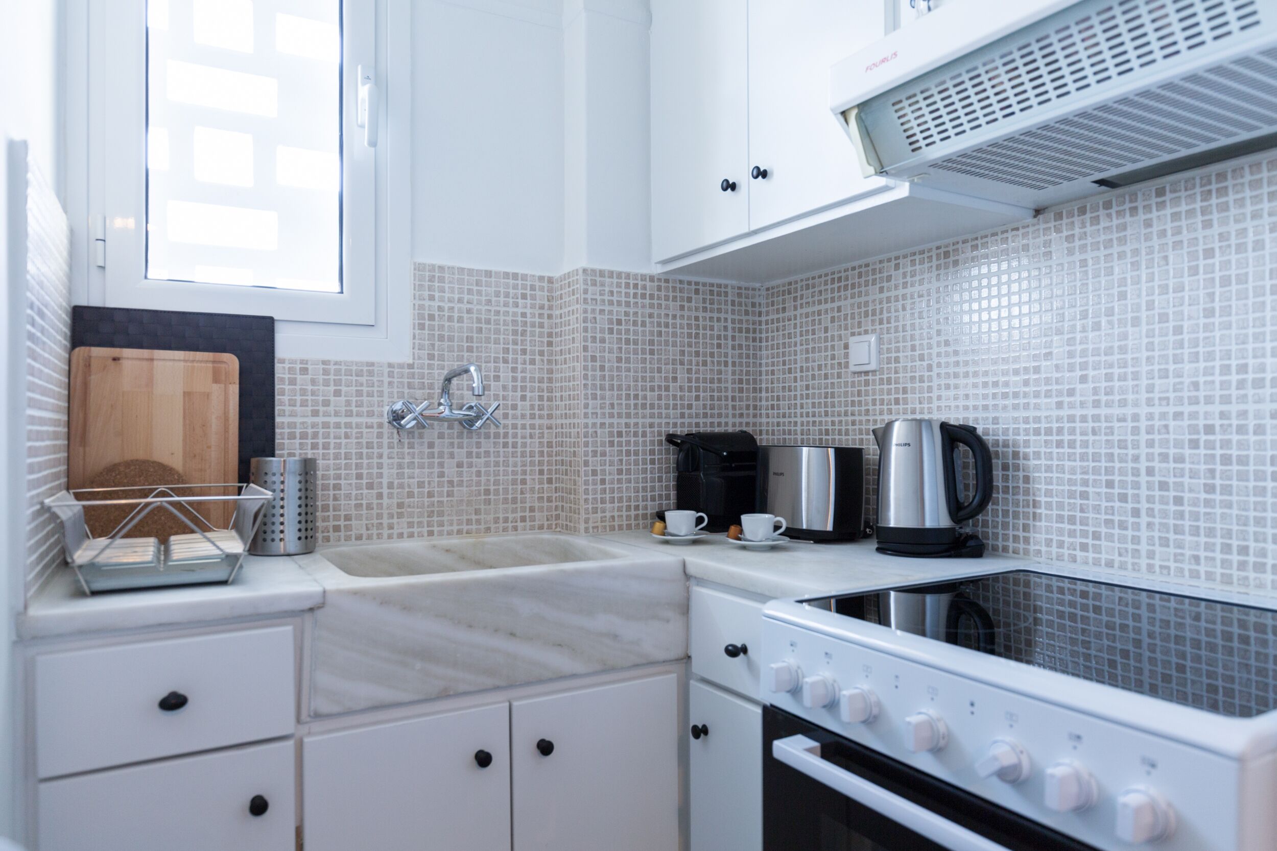 A modern kitchen with white cabinets, a sink, a stove, and a window.