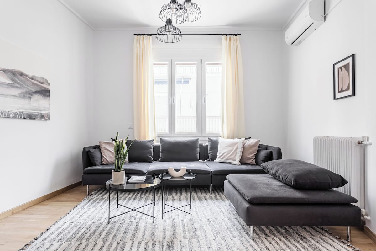 A modern living room with a dark sofa, a round coffee table, and a large window with curtains.